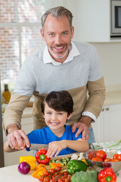 Vader die een zoon bijstaat om de rode groene paprika in keuken te hakken