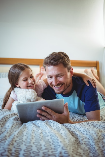 Vader die met dochter op bed ligt en digitale tablet gebruikt