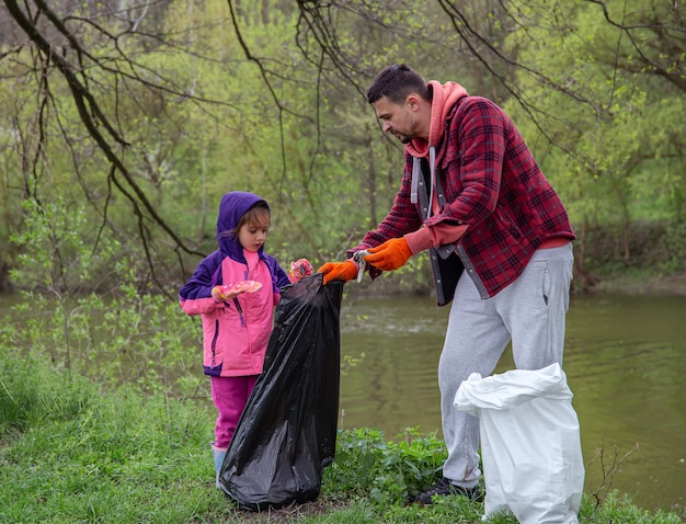Vader en dochter, met vuilniszakken, maken de omgeving schoon van afval.