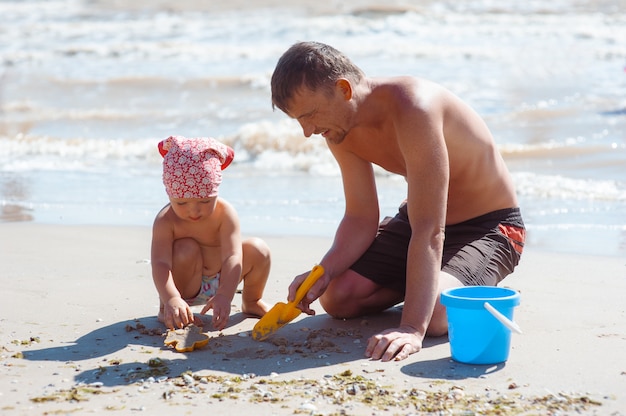 Vader en dochter op strand spelen en zand kasteel bouwen