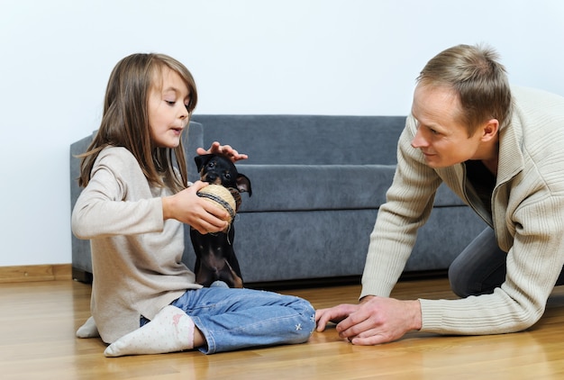 Vader en dochter spelen met de puppy's op de vloer in de kamer. het meisje geeft de bal aan de hond.