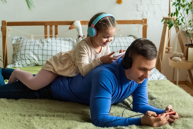 Vader en dochter spelen samen op smartphone met een koptelefoon thuis Goede ouder- en kindrelaties