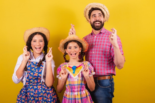 Vader en dochters dragen typische kleding voor de Festa Junina met gekruiste vingers die hoopvol wensen voor het Arraia-feest