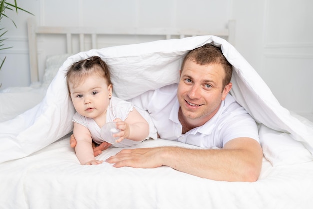 Vader en dochtertje op het bed onder de deken glimlachend en knuffelend gelukkige familie vaderdag