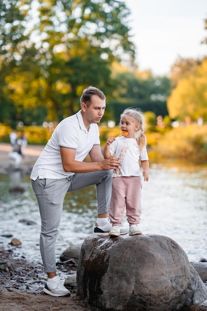 Vader en kleine schattige blonde dochter samen in de zomer in het park in de natuur klein meisje dat lolly eet