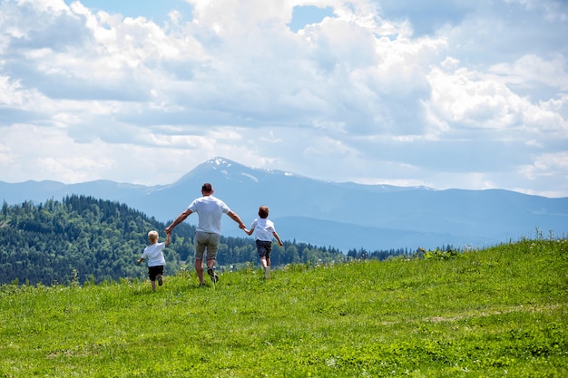Vader en twee jonge zonen die op het groene veld hand in hand lopen