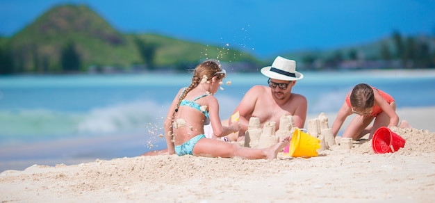 Vader en twee meisjes die met zand op tropisch strand spelen