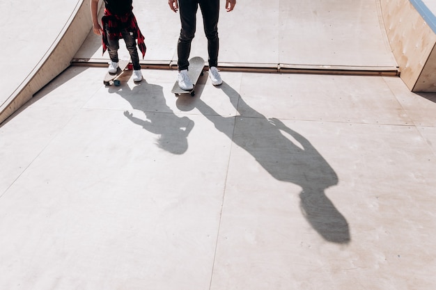 Vader en zijn zoontje gekleed in de vrijetijdskleding rijden skateboards in een skatepark met glijbanen op de zonnige dag.