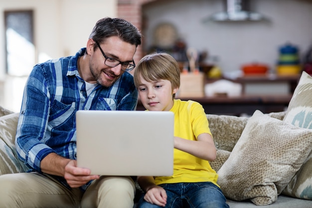 Vader en zoon die laptop in woonkamer met behulp van