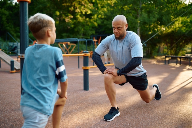 Vader en zoon doen oefening, sporttraining op speelplaats buiten. Het gezin leidt een gezonde levensstijl, fitnesstraining in het zomerpark