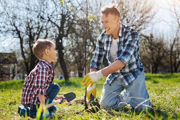 Vader en zoon dragen allebei een geruite korte broek die glimlachen terwijl ze een nieuwe boom in een familietuin zetten