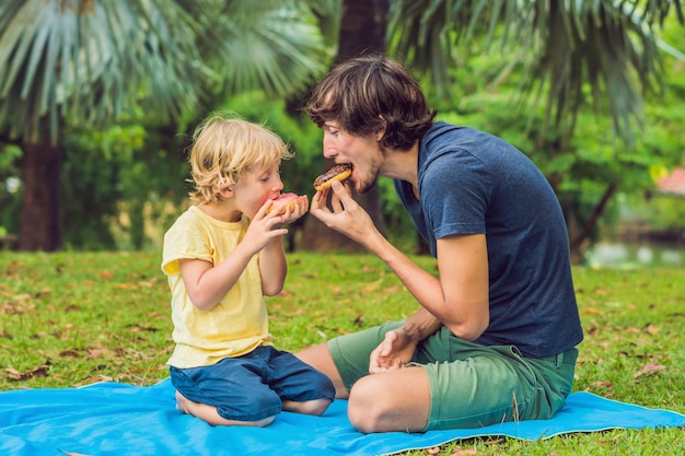 Vader en zoon eten een donut in het park. Schadelijke voeding in het gezin.