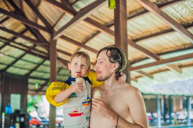 Vader en zoon eten van ijs in aquapark onder een rieten dak