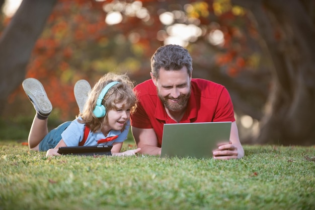 Vader en zoon gebruiken laptop voor video-oproep of les luisteren muziek in koptelefoon in park srudy online