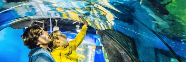 Vader en zoon kijken naar de vissen in het aquarium in oceanariumbanner lang formaat