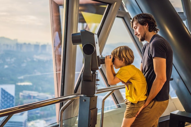 Vader en zoon kijken naar het stadsbeeld van Kuala Lumpur Gebruik een verrekijker Panoramisch uitzicht op de skyline van de stad van Kuala Lumpur 's avonds bij zonsondergang wolkenkrabbers bouwen in Maleisië Reizen met kinderen concept