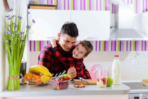 Vader en zoon knuffelen in een keuken. Zittend aan de tafel vol met vers fruit.