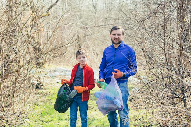 Vader en zoon maken het vuilnispark schoon Vrijwilligers maken het bos schoon van plastic flessen en brengen samen tijd door