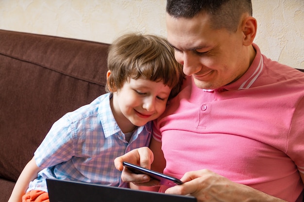 Vader en zoon met laptop en mobiele telefoon thuis