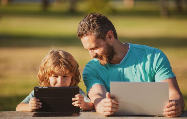 Vader en zoon met laptop en tablet online leren kind met een laptop buiten in de zomer kind