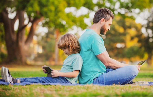 Vader en zoon met laptop in park, papa leert kind moderne technologie voor afstandsonderwijs gebruiken