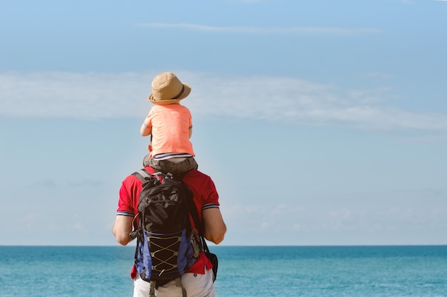 Vader en zoon op hun schouders staan op de kust, achteraanzicht