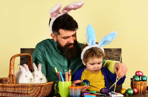 Vader en zoon schilderen paaseieren schattige kleine kindjongen met konijnenoren op paasdag gelukkig