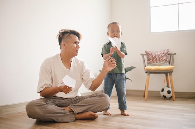 Vader en zoon spelen met papieren vliegtuigjes en glimlachen terwijl ze samen tijd doorbrengen thuis