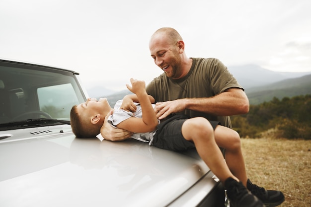 Vader en zoon spelen op de motorkap van een auto tijdens een roadtrip