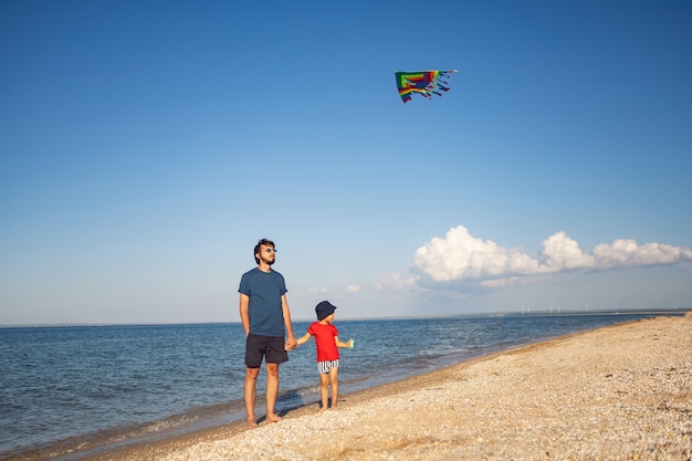 Vader en zoon staan op een zandstrand aan zee en lanceren in de zomer op vakantie een gestreepte speelgoedvlieger