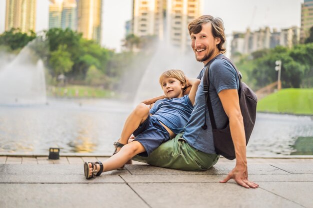 Vader en zoon toeristen op de achtergrond van de fontein op het meer 's nachts in de buurt van Twin Towers met stad op de achtergrond Kuala Lumpur, Maleisië