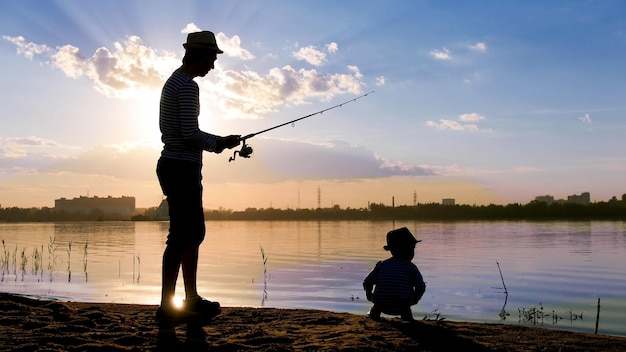 Vader en zoon vissen aan de oever van de rivier in de stralen van de zonsondergang