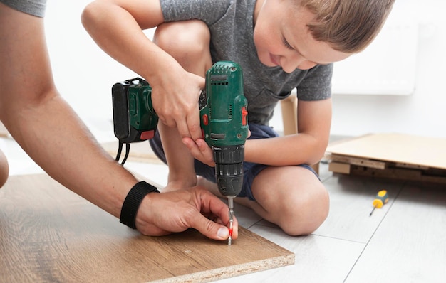 Foto vader en zoon zetten het bureau in elkaar en vader leert zijn zoon hoe hij gereedschap moet gebruiken