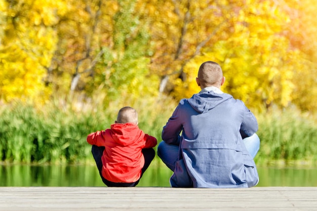 Vader en zoon zitten op het dok herfst zonnig achteraanzicht