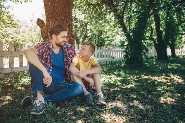 Vader en zoon zitten samen onder de boom en kijken elkaar aan