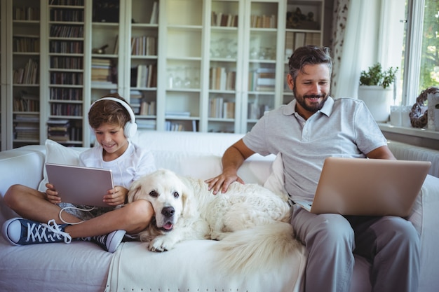 Vader en zoon zittend op een bank en het gebruik van digitale tablet en laptop