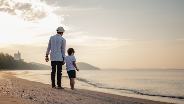 Vader houdt hun kind de hand vast en loopt op het strand bij zonsondergang in vakantie Holiday Family