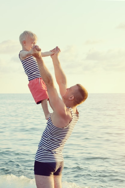 Vader houdt zijn zoon in uitgestrekte handen op de zeekust. Veel plezier