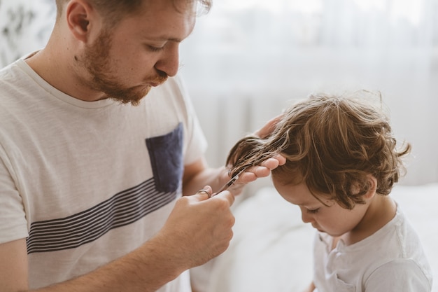 Vader knipt het haar van haar zoon in de kamer. Familie tijdens quarantaine