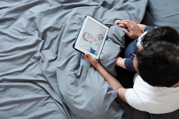 Vader knuffelt zijn kind als ze in bed zitten en videobellend arts om griepbehandeling te bespreken