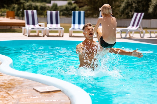 Vader lacht terwijl hij zijn zoon in het water gooit