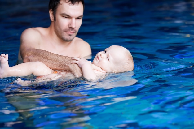 Vader leert baby zwemmen in de klas in een zwembad