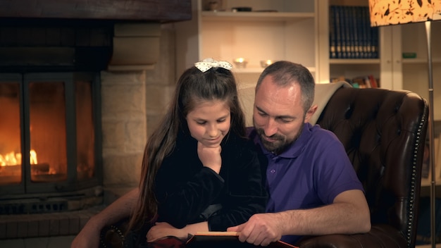 Vader leest zijn kleine meisje een sprookje bij de open haard