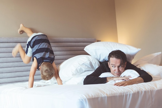 Vader ligt terwijl zoon thuis op het bed speelt