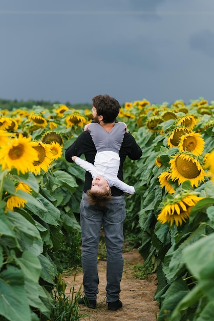 Vader met een jonge zoon op zijn schouders, wandelen en plezier maken in een veld met zonnebloemen