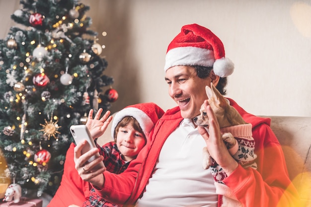 Vader met kind en puppyhond in kerstmanhoeden die een videochat hebben