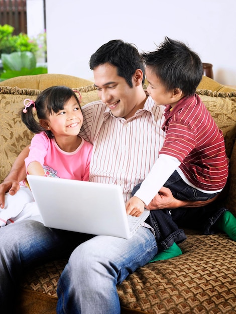 Vader met kinderen die thuis een laptop op de bank gebruiken