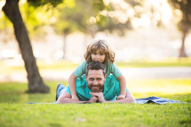 Vader met schattige kindjongen die op gras ligt in het zomerpark buiten, vader en zoon ontspannen op de natuur