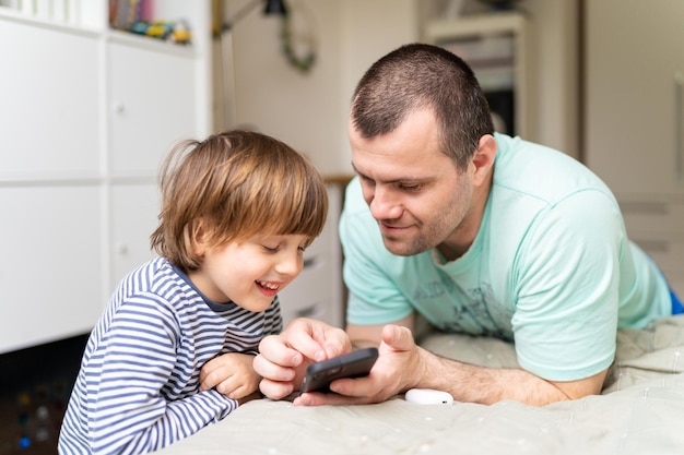 Vader met voorschoolse zoon die smartphone thuis gebruikt vader die tijd doorbrengt met kinderen die grappige foto's en video's op zijn telefoon laten zien