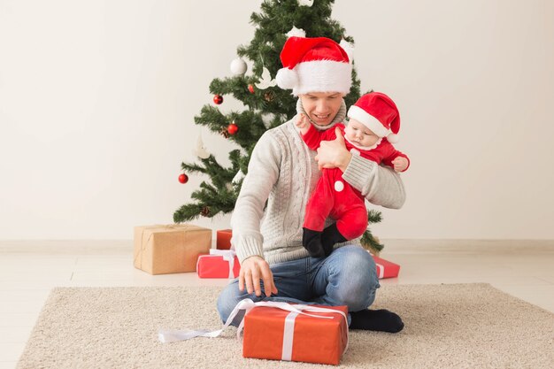 Vader met zijn grappige babyjongen die Kerstmanhoeden draagt die Kerstmis vieren.